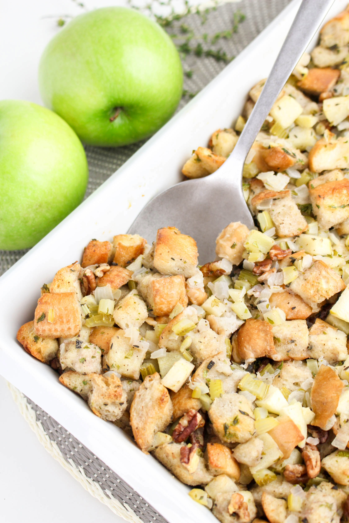 A stainless steel spoon scooping apple stuffing with herbs and pecans.