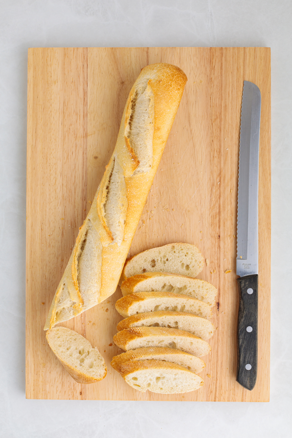 A baguette on a cutting board with sliced bread cut in a diagonal.