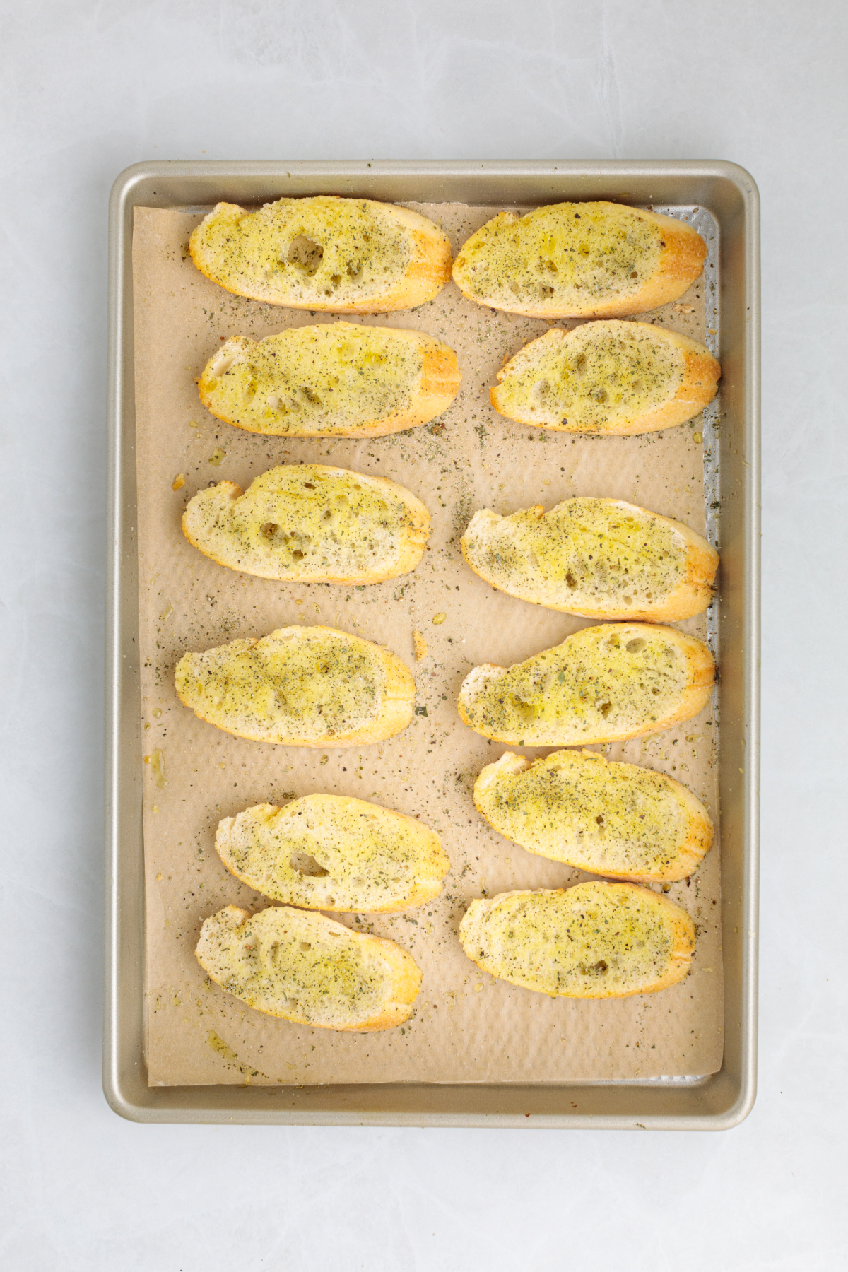 Seasoned sliced baguette on a baking sheet before toasting.