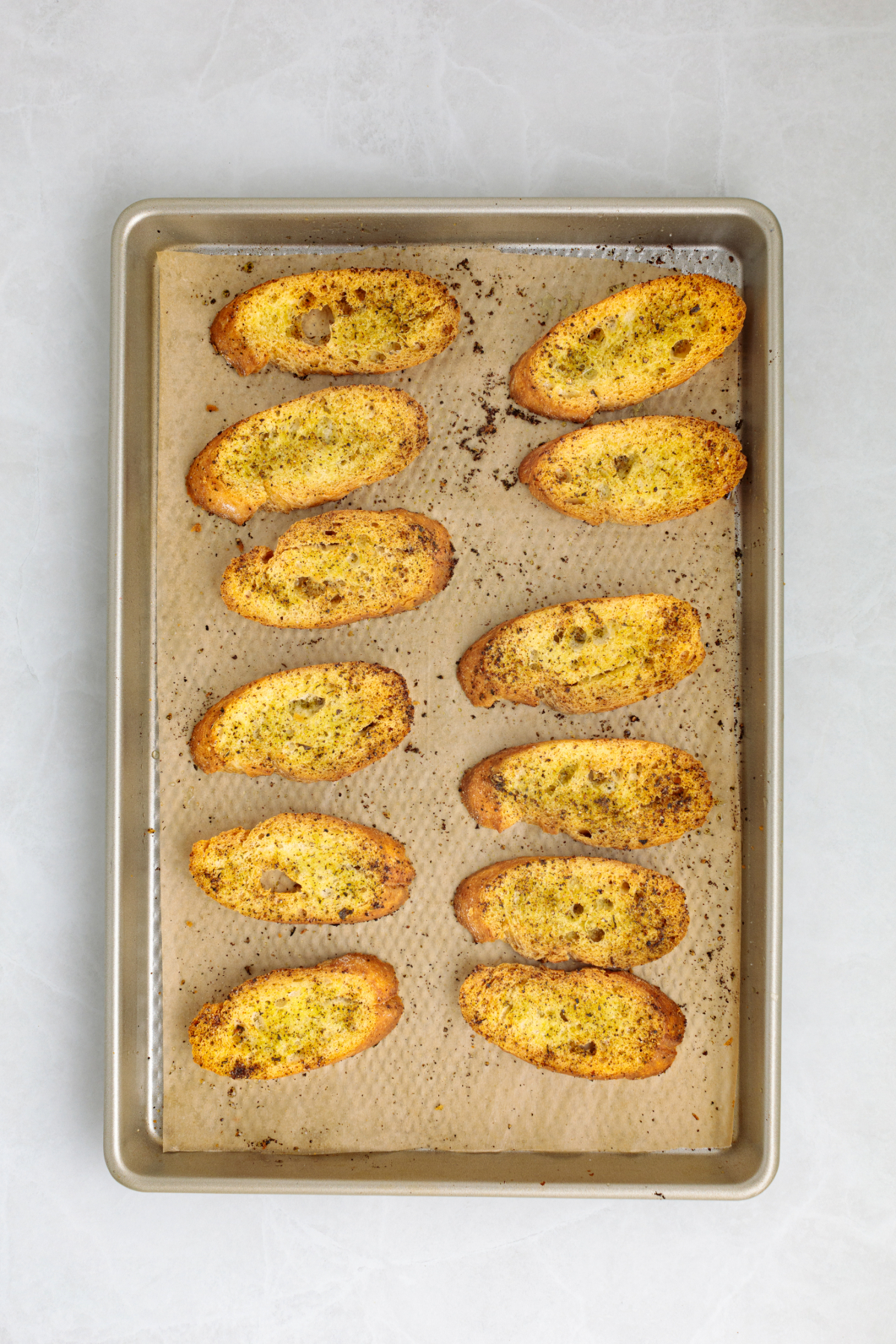 Toasted baguette crackers on a stainless baking sheet after removing from the oven.