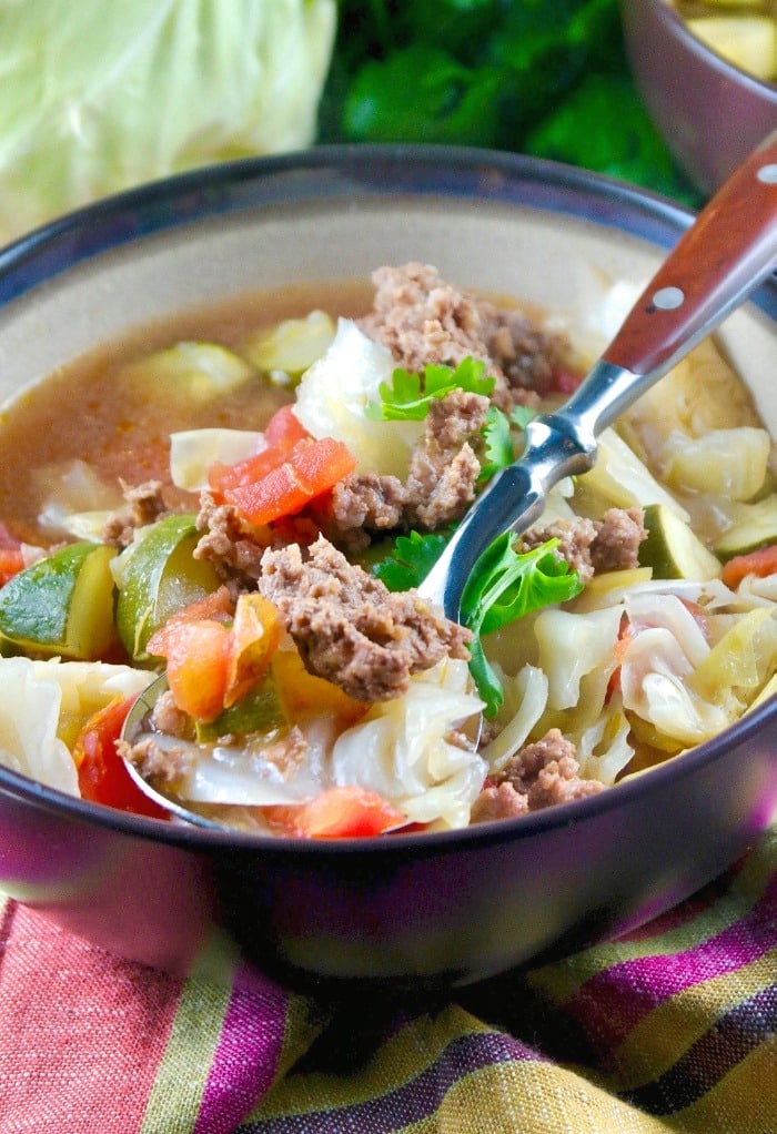bowl of beef cabbage soup with a a wooden handle spoon