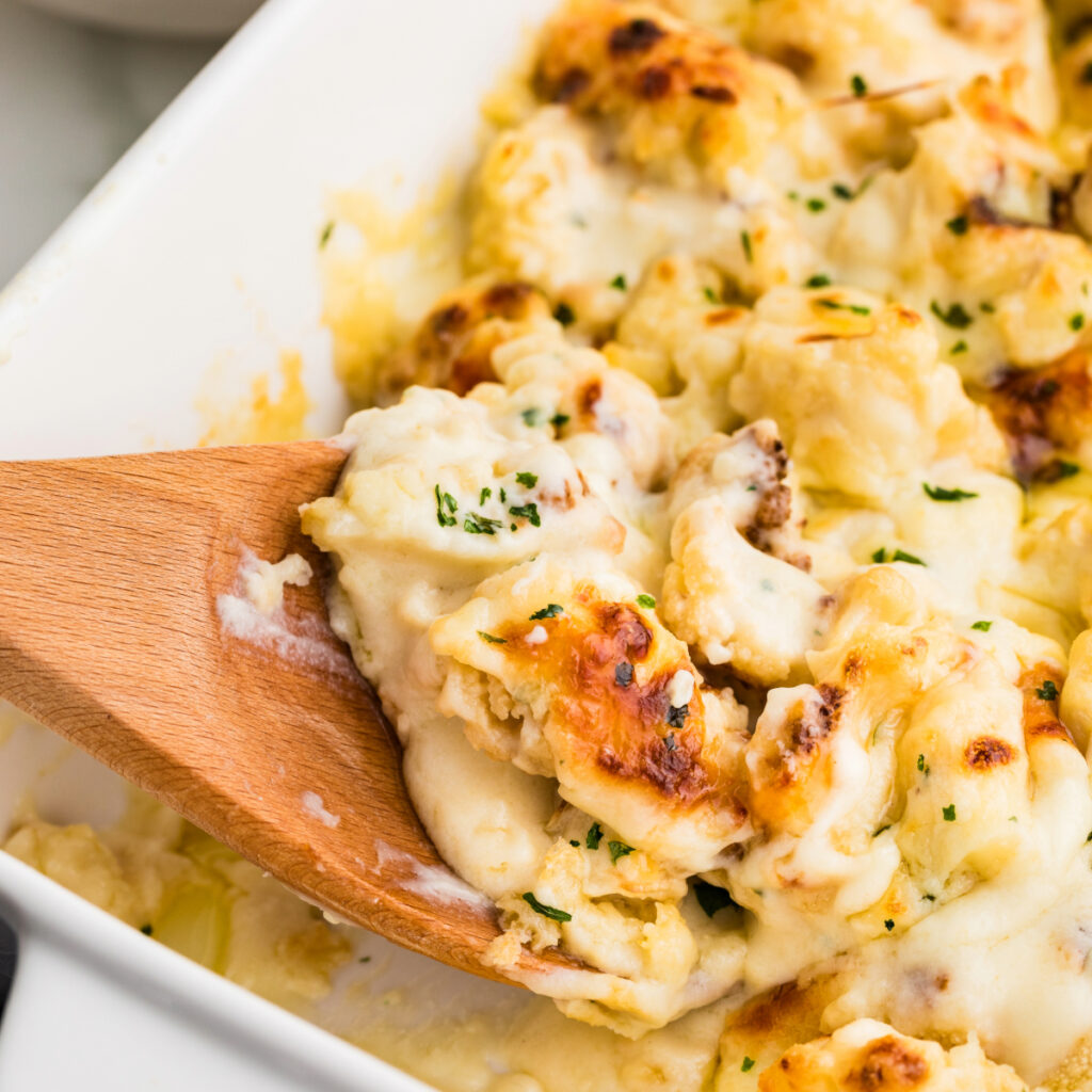 A wooden spoon of cauliflower baked with a cheese sauce.