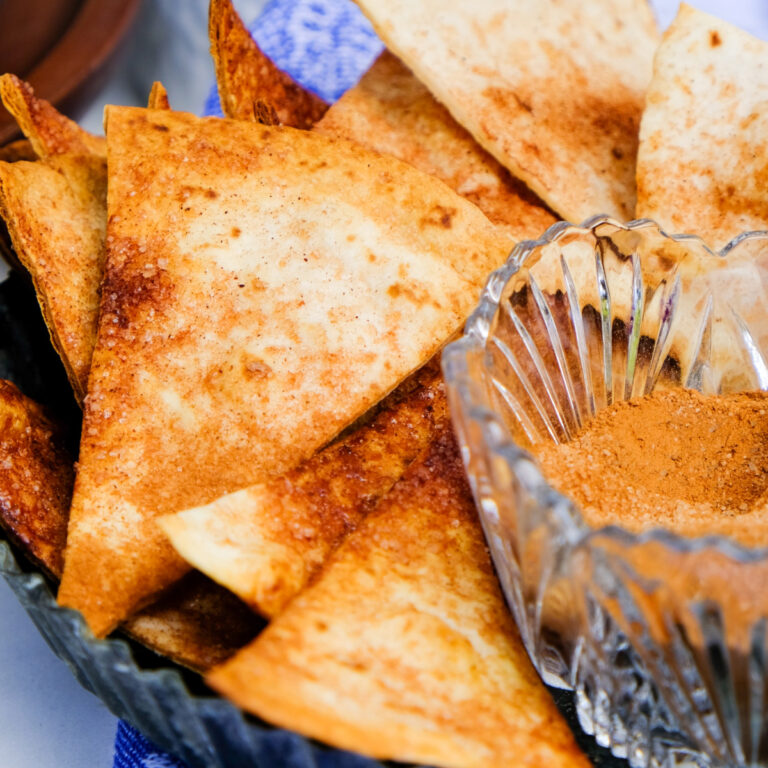 Baked cinnamon tortilla chips with cinnamon sugar mix on the side in a clear glass bowl.