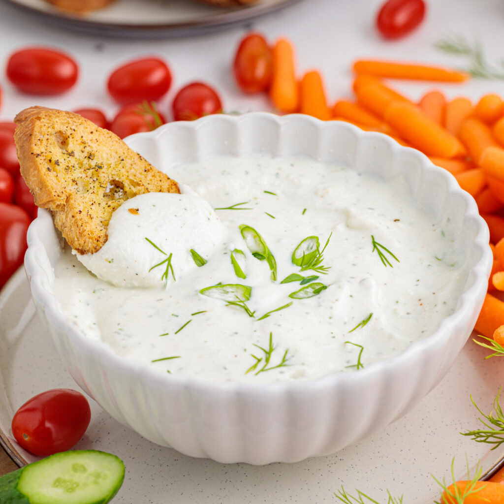 Cottage cheese ranch dip in a white bowl with a cracker dipped in the dip.