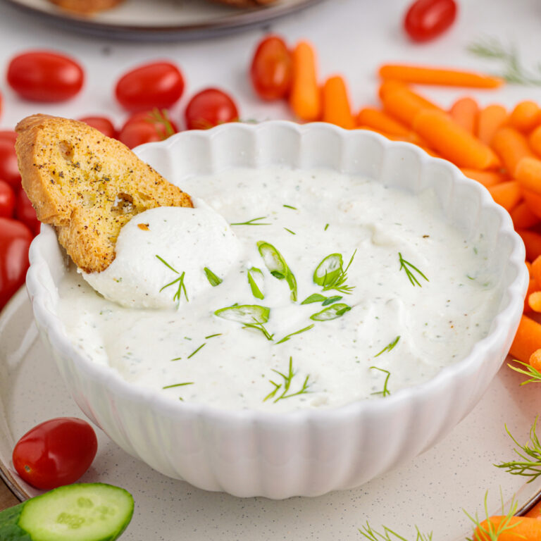 Cottage cheese ranch dip in a white bowl with a cracker dipped in the dip.