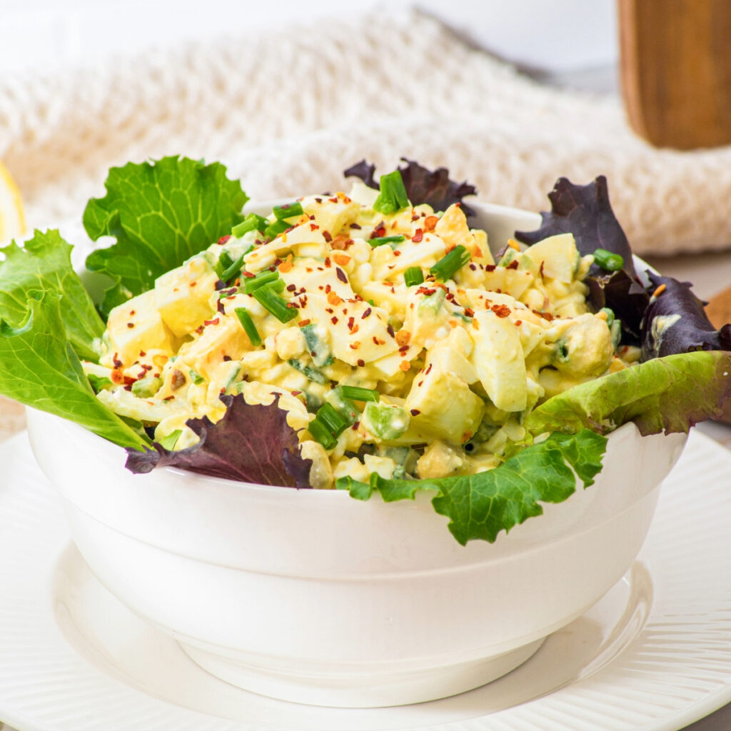 Egg salad in a white bowl lined with lettuce leaves.
