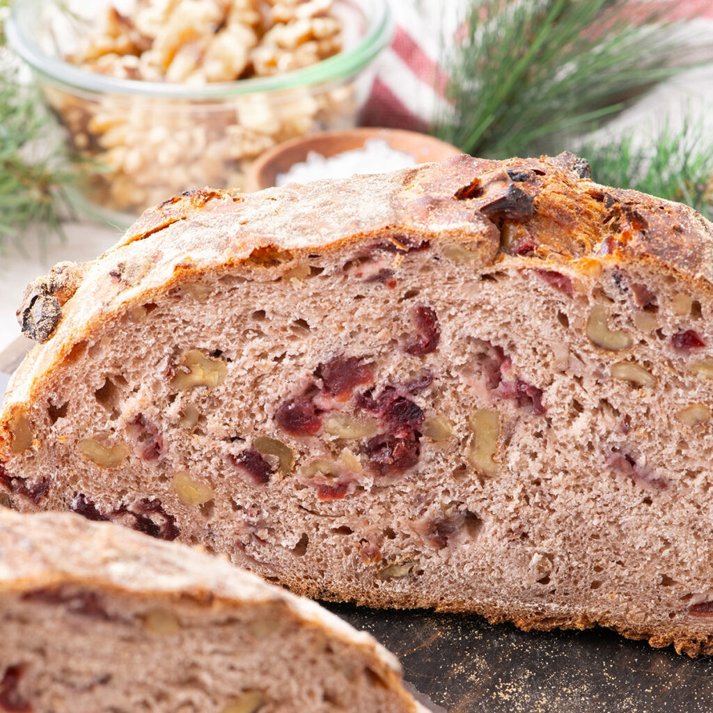 A loaf of cranberry walnut bread sliced exposing the center on a cutting board.