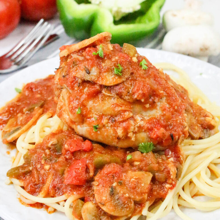 Chicken cacciatore over spaghetti on a white dinner plate.