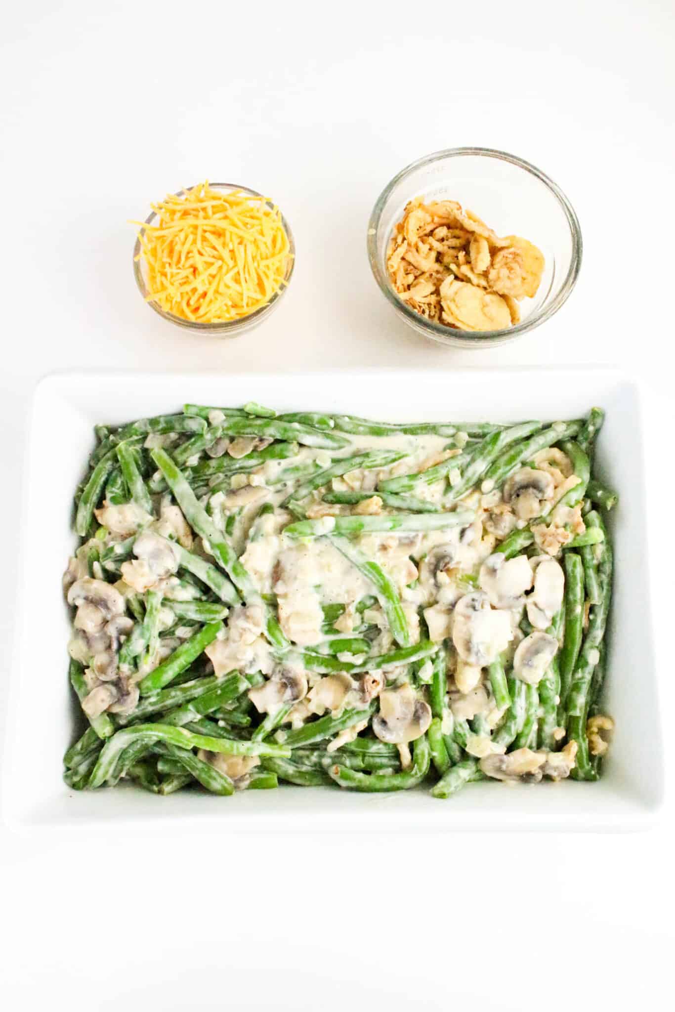 Fresh green beans topped with sauce and mushrooms in a white baking dish.