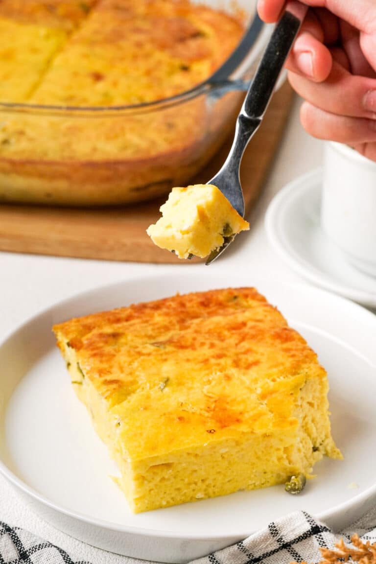 Slice of green chile egg casserole on a white dish with a fork taking a bite off.