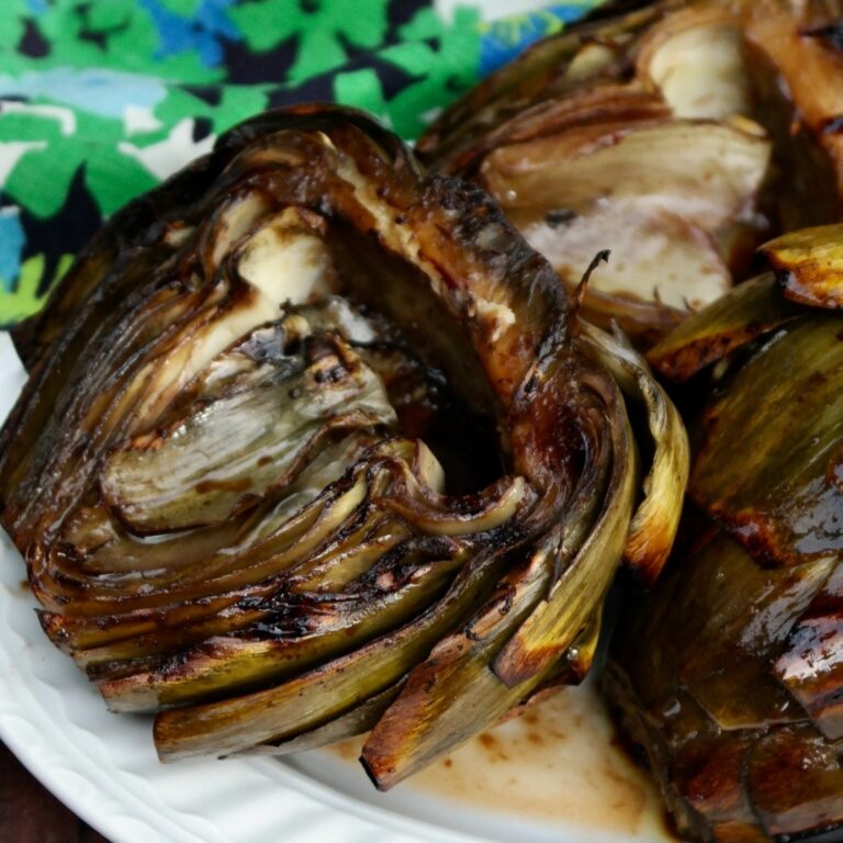 Grilled artichokes on a white serving plate.