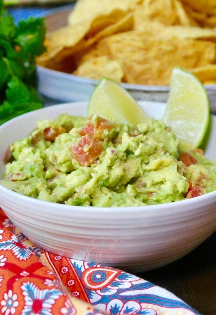 guacamole dip in a white bowl with slices of lime
