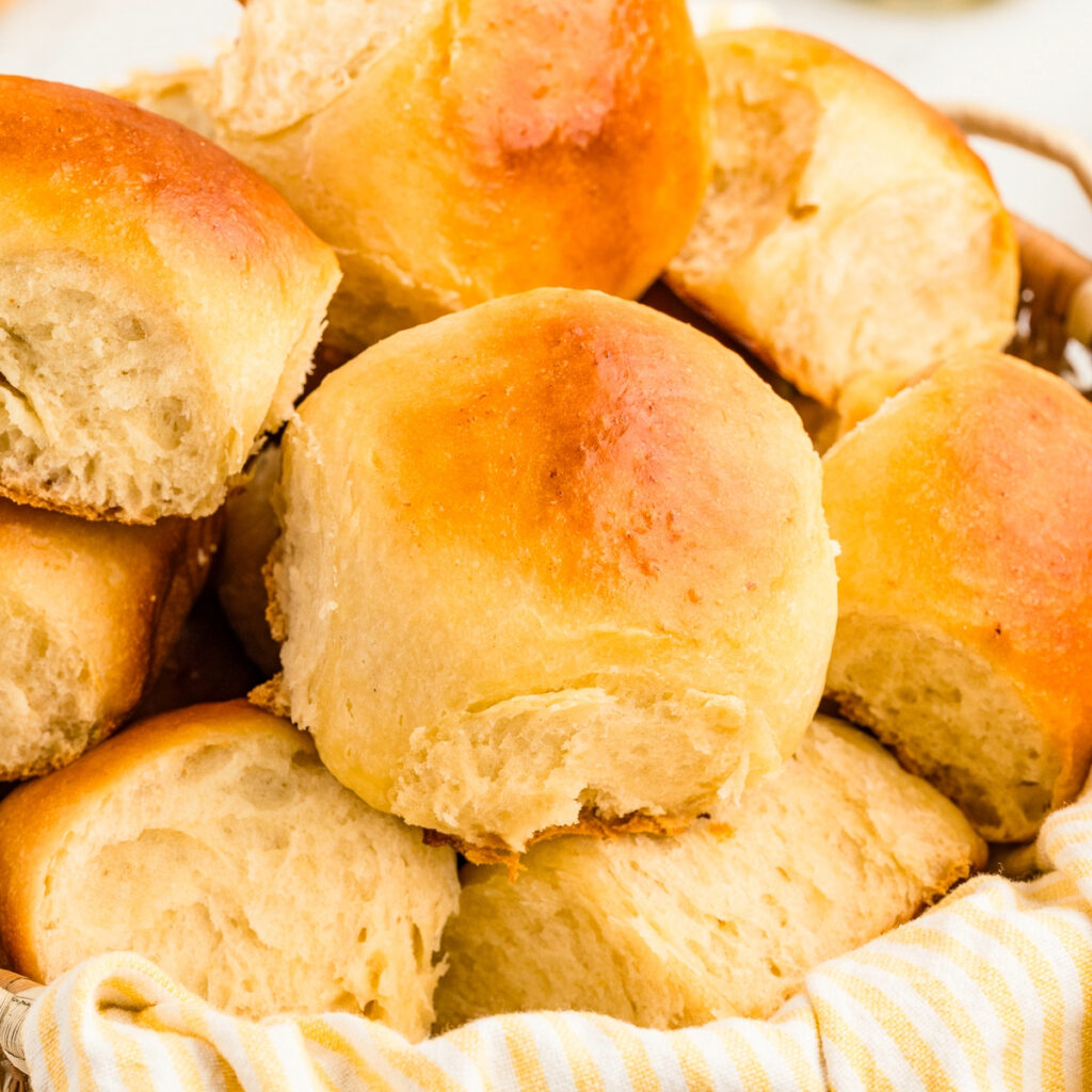 Homemade Hawaiian rolls in a basket with a kitchen towel.
