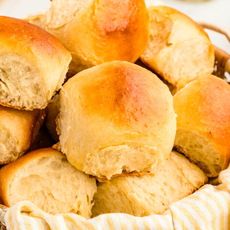 Homemade Hawaiian rolls in a basket with a kitchen towel.