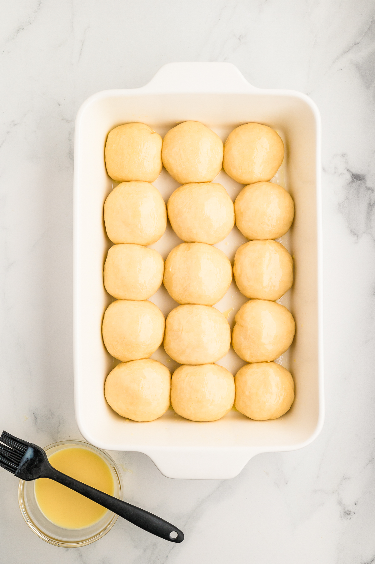 Second rise proofed Hawaiian rolls before baking with melted butter on the side with a pastry brush.