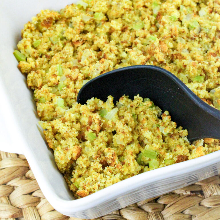 Cornbread dressing being scooped out of a casserole dish.