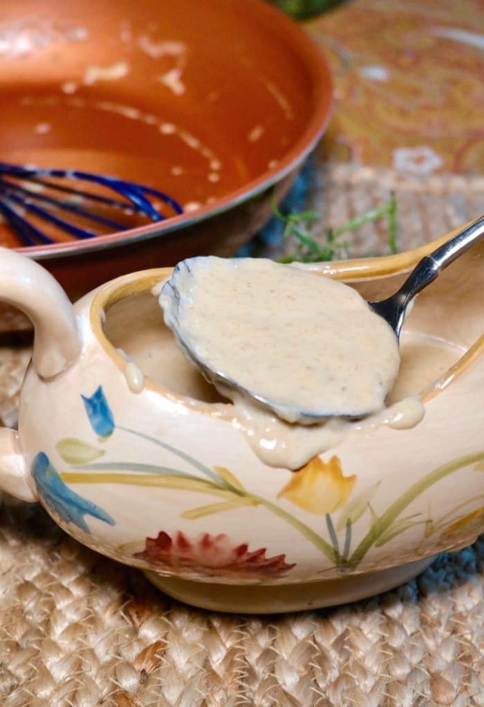 White low carb keto gravy in a gravy serving dish with a spoon scooping it out of the dish