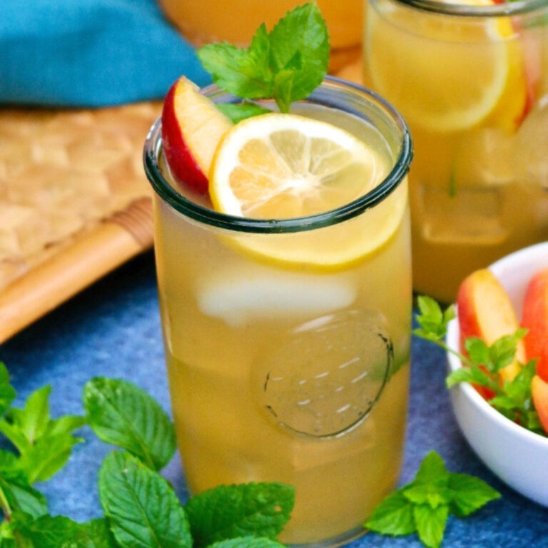 Peach lemonade in a clear glass with a slice of peach and lemon.