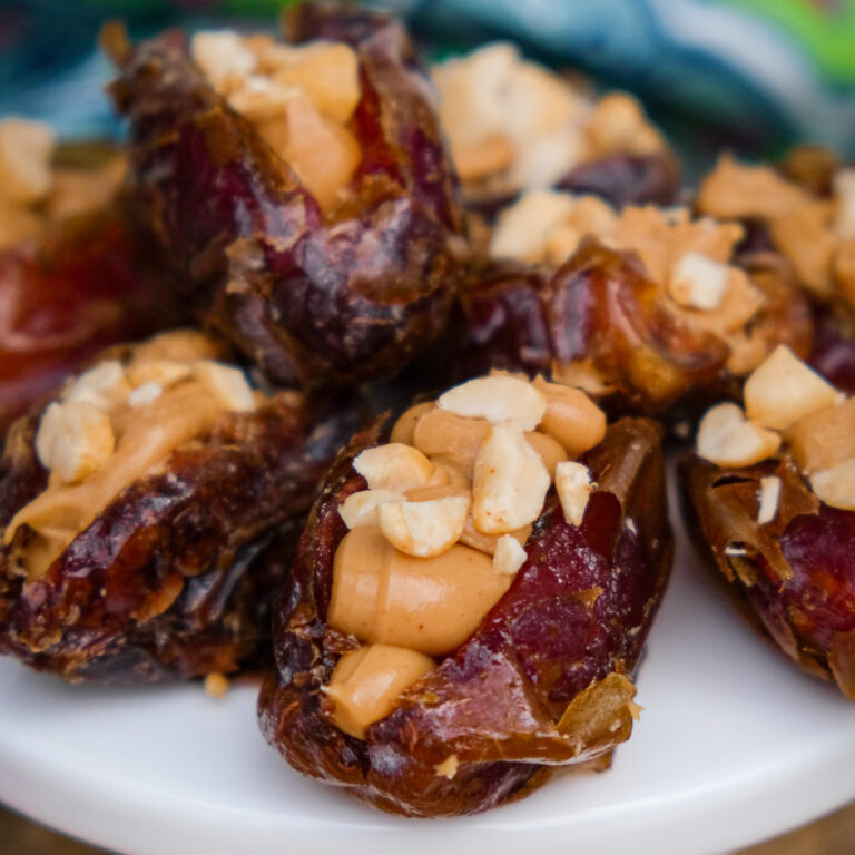 Dates stuffed with peanut butter and topped with chopped peanuts on a small white pedestal plate.