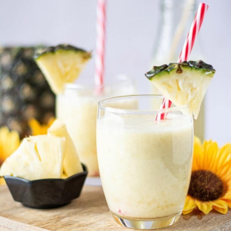 Homemade protein smoothie with pineapple in a clear glass with a stripped straw.