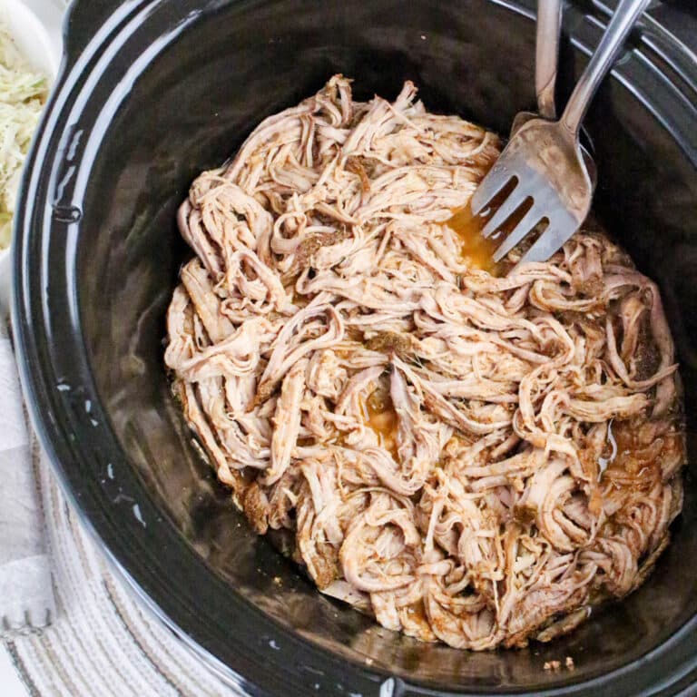 Top view of pulled pork with two forks in a slow cooker.
