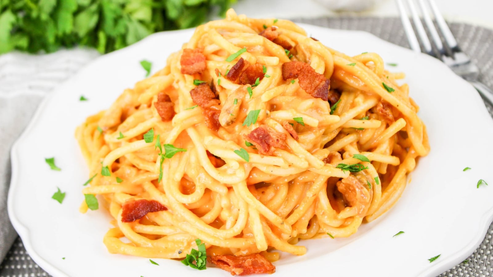 A plate of spaghetti carbonara topped with bacon bits and herbs, set on a white plate with a fork.