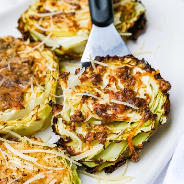 Roasted cabbage steaks topped with parmesan cheese on a white serving platter.