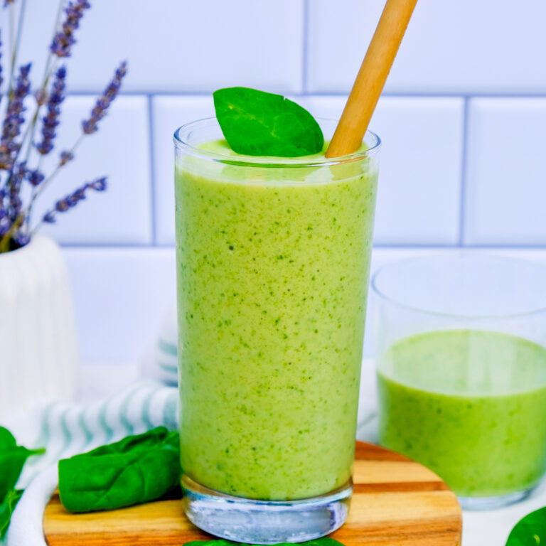 Healthy spinach avocado smoothie in a tall glass with fresh spinach on the side.