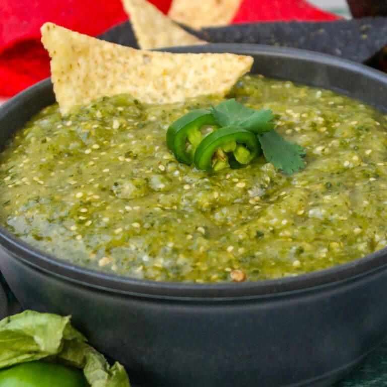 Green salsa in a black bowl with a tortilla chip and slice of jalapeno.