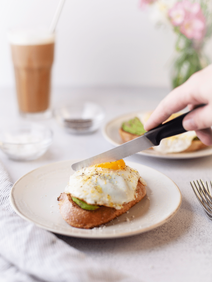 Serrated knife ready to slice into an egg on top of toast and avocado slices.