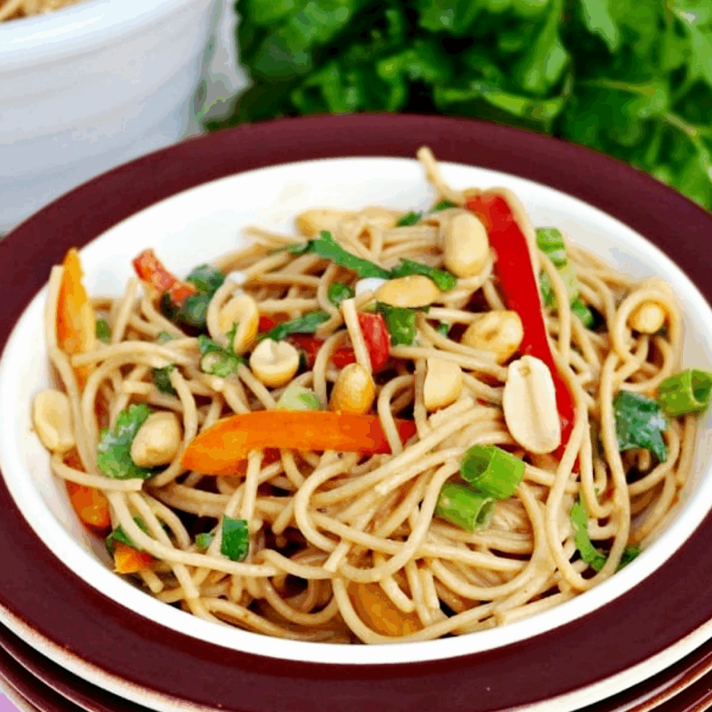 Thai style noodles with peanut sauce with vegetables in a bowl with a brown rim.